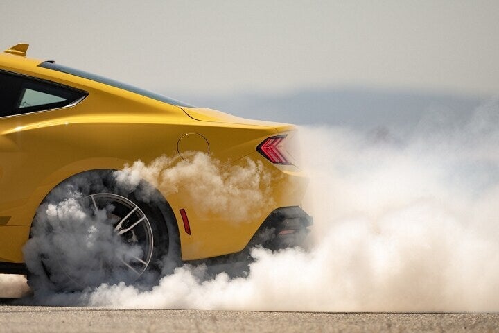 Yellow Ford Mustang performing burnout with smoke